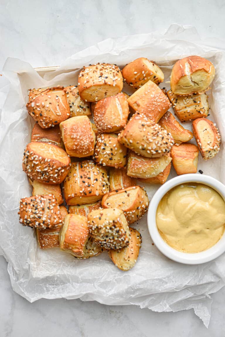 The sourdough pretzel bites are on a square plate with a bowl of mustard on the plate.