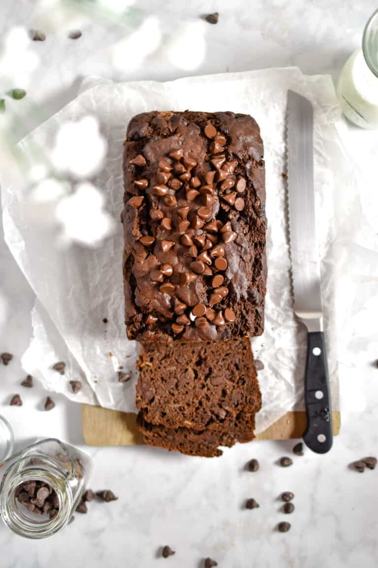 The double chocolate banana bread is on a cutting board with a knife and flowers around it