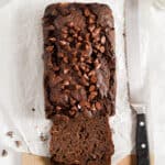 A knife is next to the double chocolate banana bread on a parchment paper lined cutting board.
