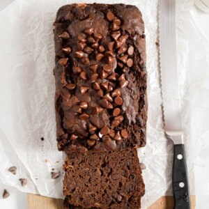 A knife is next to the double chocolate banana bread on a parchment paper lined cutting board.