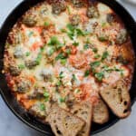 A blue kitchen towel is wrapped around the handle of the skillet with the meatball sub dip.