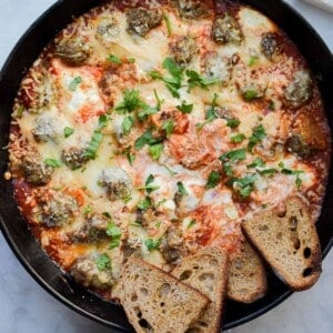 A blue kitchen towel is wrapped around the handle of the skillet with the meatball sub dip.