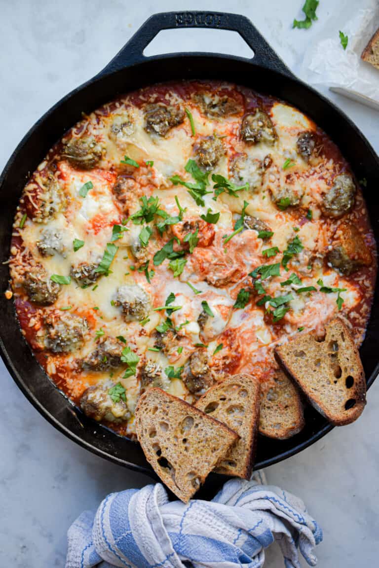 A blue kitchen towel is wrapped around the handle of the skillet with the meatball sub dip.