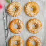 Six peach kefir doughnuts are laid out on a parchment paper on top of a wire rack.