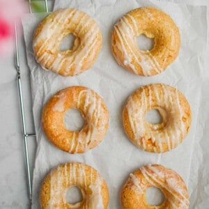 Six peach kefir doughnuts are laid out on a parchment paper on top of a wire rack.