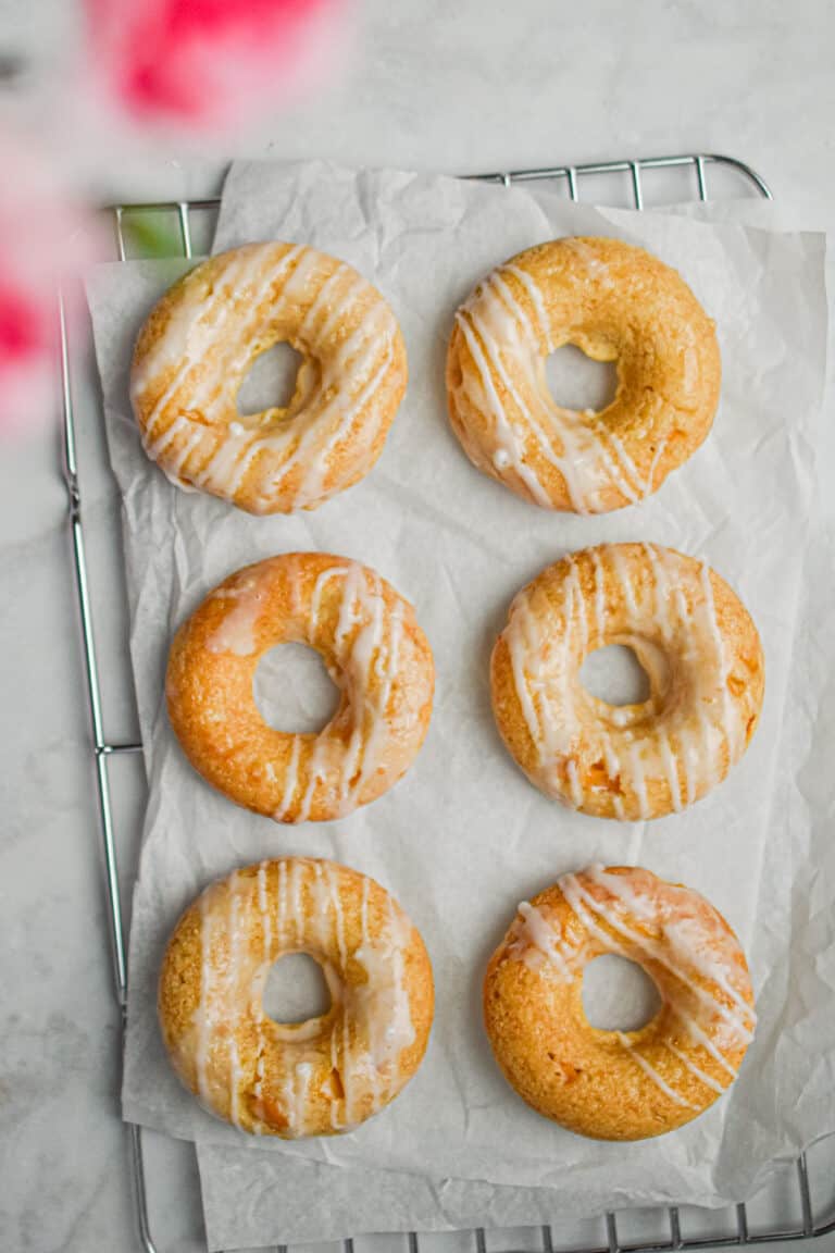 Six peach kefir doughnuts are laid out on a parchment paper on top of a wire rack.