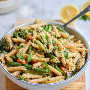 A bowl of pasta is on a cutting board with a lemon in the back