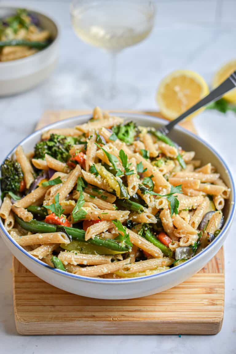 A bowl of pasta is on a cutting board with a lemon in the back
