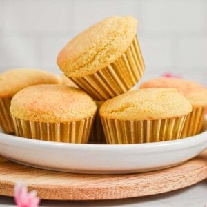 One muffin is on top of four other muffins on a plate.