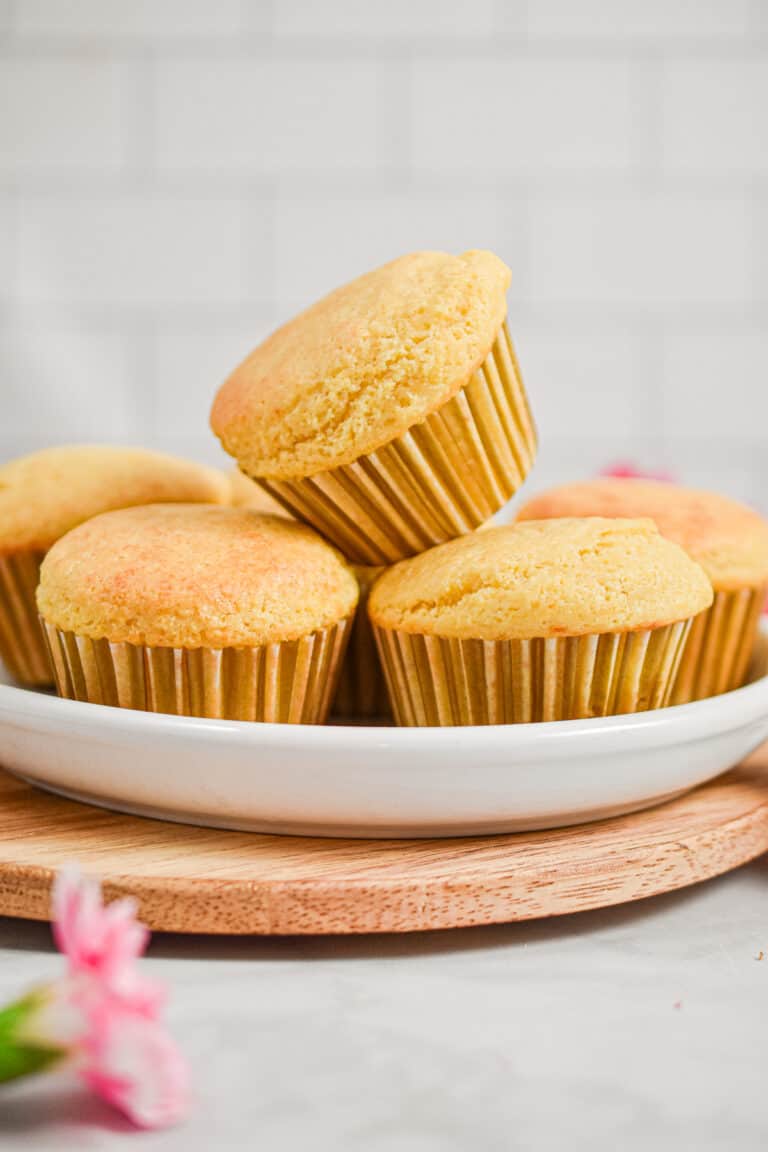 One muffin is on top of four other muffins on a plate.