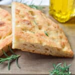 The sourdough focaccia is cut in half and on a wooden cutting board with an olive oil bottle in the background.
