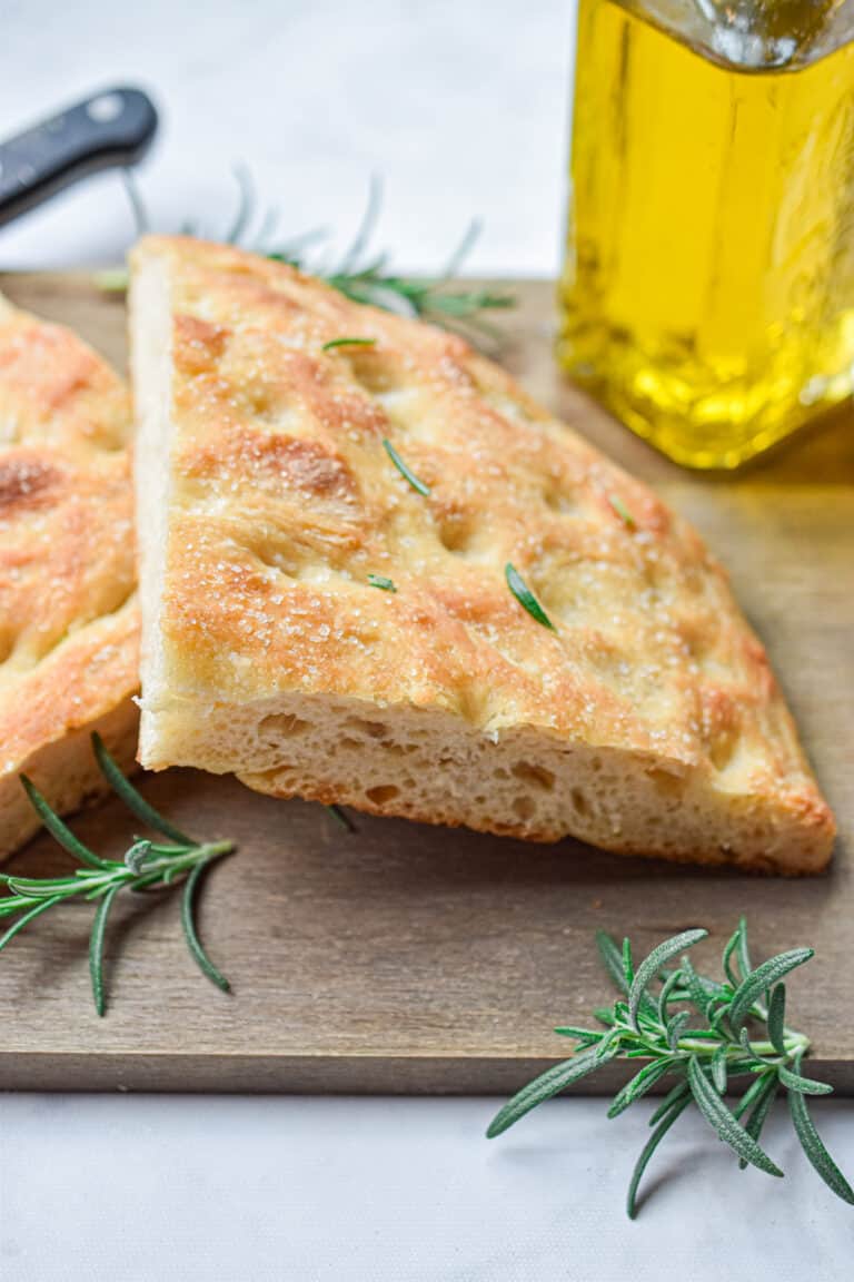 The sourdough focaccia is cut in half and on a wooden cutting board with an olive oil bottle in the background.
