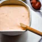 A spoon of sriracha is in the background of the dip