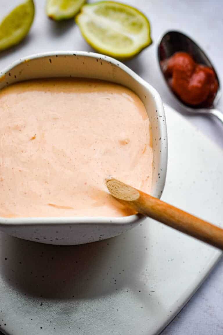 A spoon of sriracha is in the background of the dip