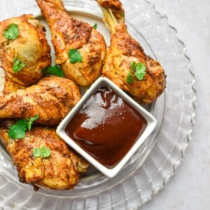 The Instant Pot Chicken Legs are on a glass plate with a bowl of barbecue sauce.