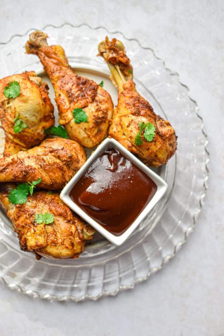 The Instant Pot Chicken Legs are on a glass plate with a bowl of barbecue sauce.