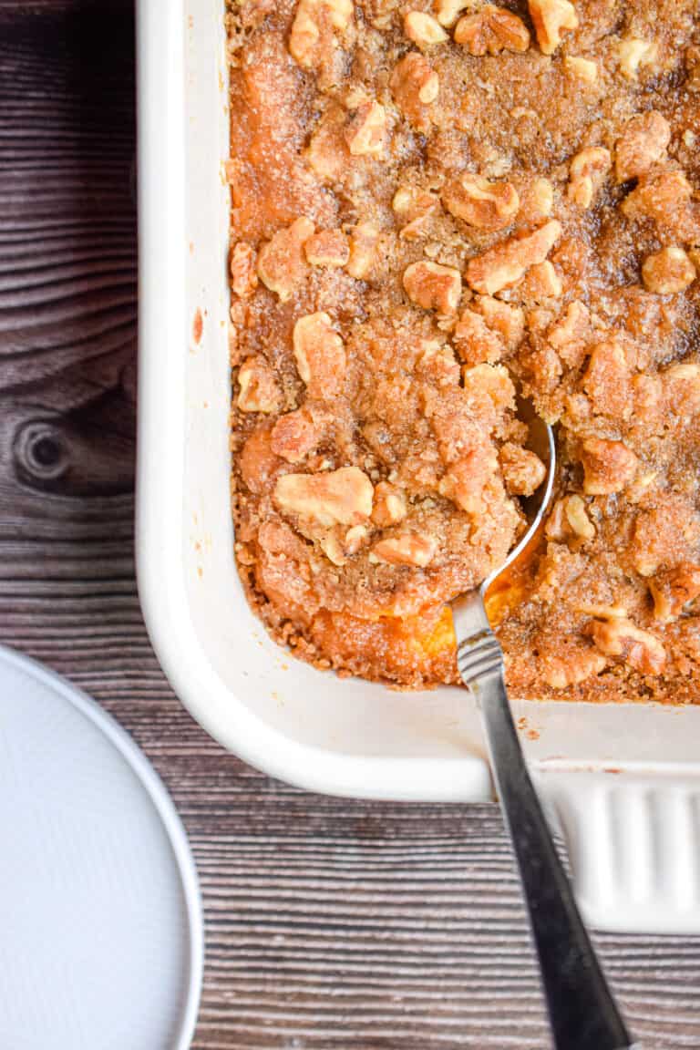 A spoon is in the sweet potato casserole with walnuts