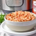 A bowl of buffalo chicken is in front of an Instant Pot and hot sauce.