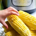 A hand is grabbing a corn on the cob.