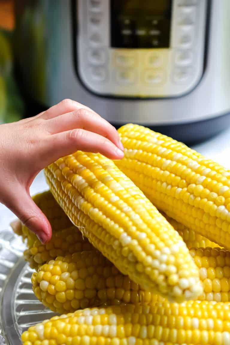 A hand is grabbing a corn on the cob.