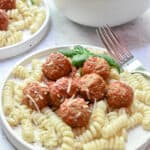A close up of a plate of pasta and meatballs with a bowl of meatballs in the background.