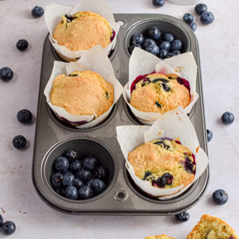 The sourdough blueberry muffins are in a 6 muffin tin with two of the pieces filled with blueberries.