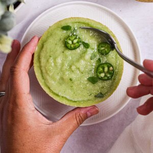 A hand is scooping the melon gazpacho.