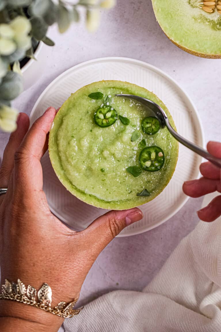 A hand is scooping the melon gazpacho.