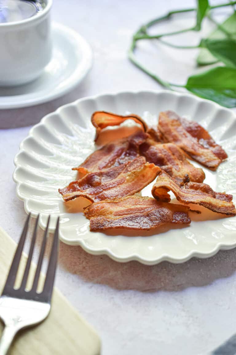 The Instant Pot Bacon is a fluted plate with a cup of coffee and leaves in the background.