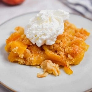The peach cobbler is on a plate with whipped cream
