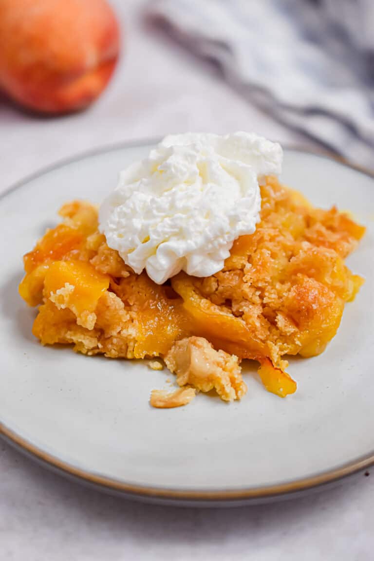 Peach cobbler is on a plate with whipped cream.