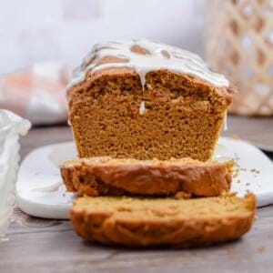 The pumpkin bread is on a cutting board with a drip of the icing coming off the front.