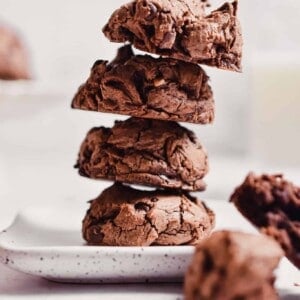 Four cookies are stacked together with a glass of milk in the back.