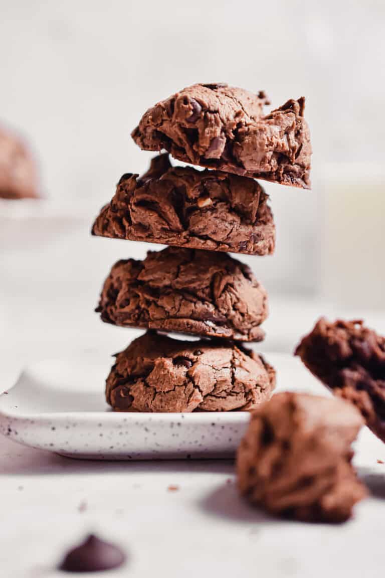 Four cookies are stacked together with a glass of milk in the back.