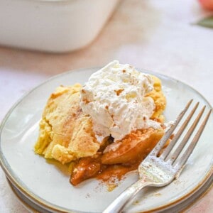A fork is on the plate with the apple cobbler and whipped cream.
