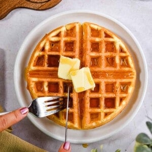 A fork and knife are cutting into the waffle.