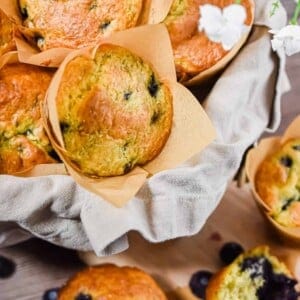 A basked of blueberries muffins are surrounded by other muffins.