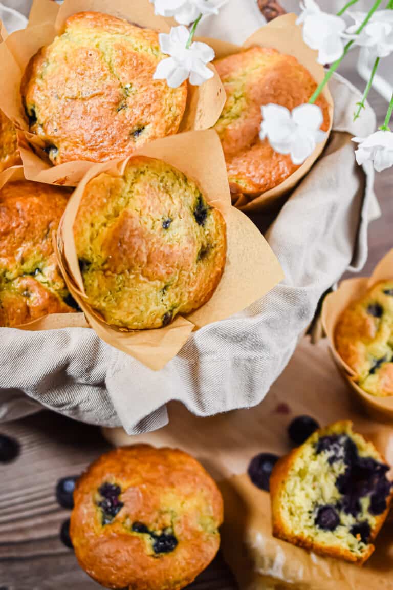 A basked of blueberries muffins are surrounded by other muffins.