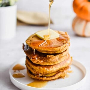 Maple syrup is being poured onto a stack of pumpkin pancakes.