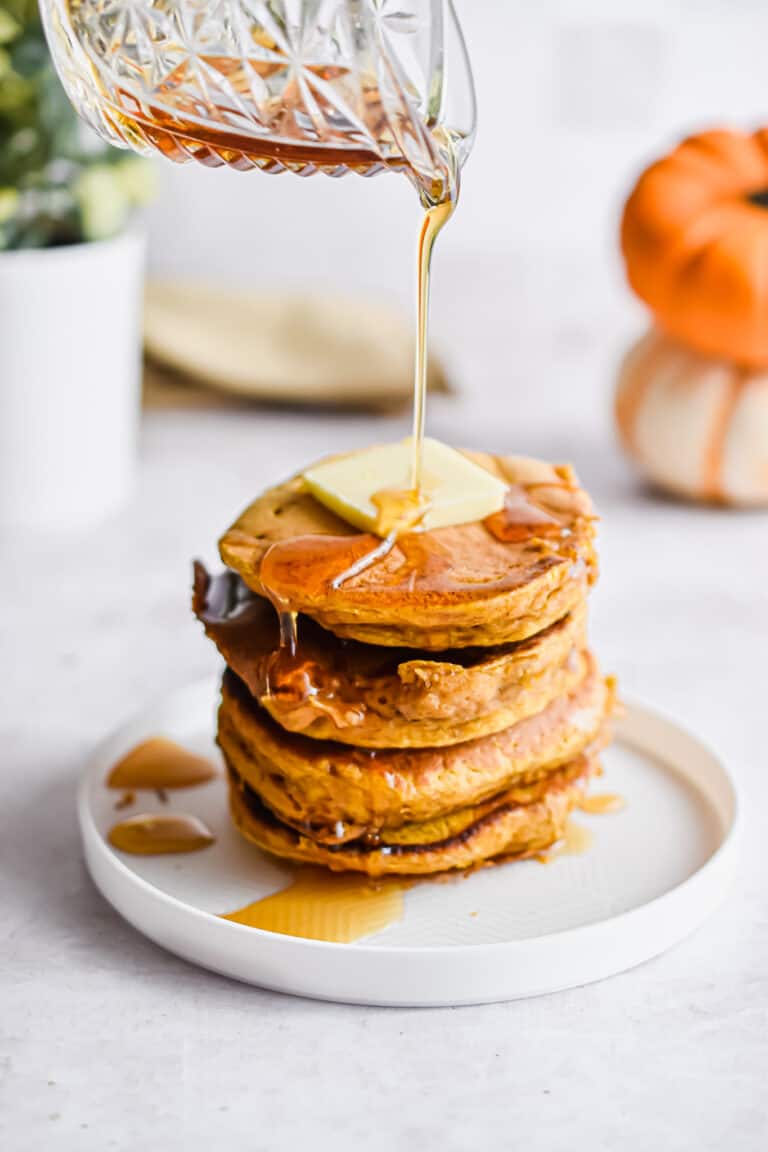 Maple syrup is being poured onto a stack of pumpkin pancakes.