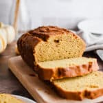 The pumpkin bread is on a cutting board and some slices are cut.
