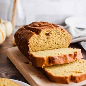 The pumpkin bread is on a cutting board and some slices are cut.
