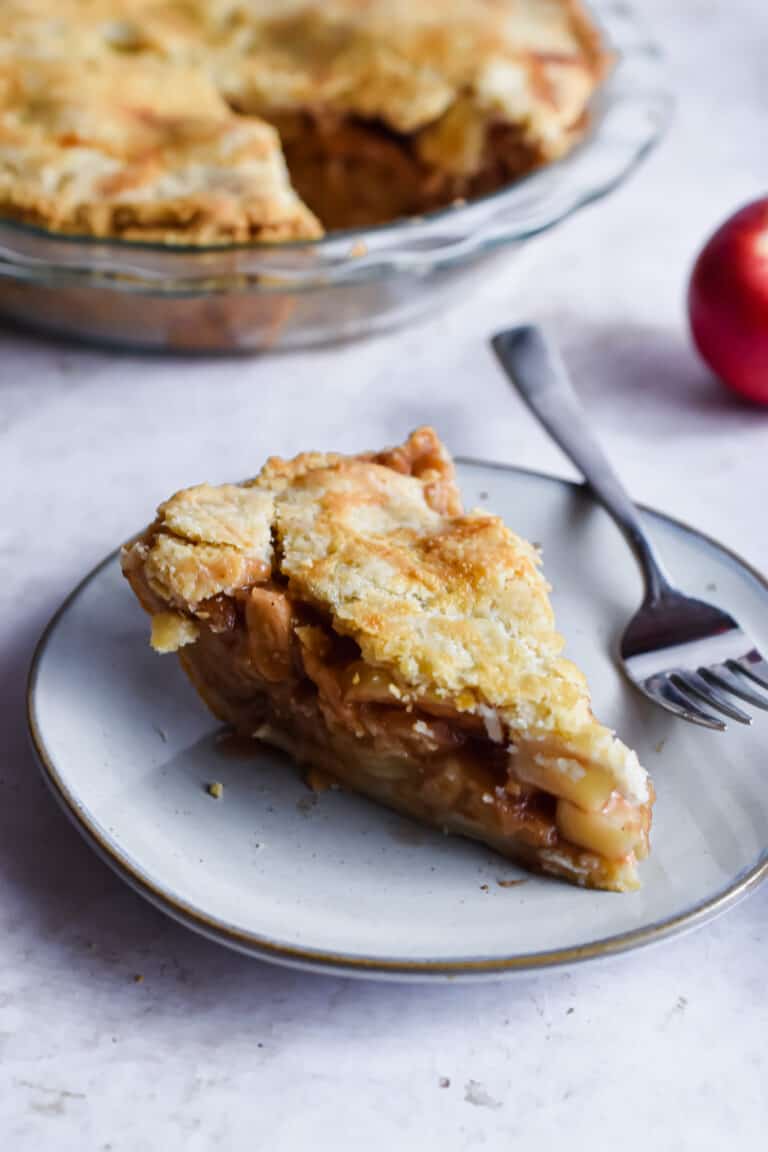A slice of apple pie is on a plate with a fork on the plate.