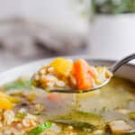 A spoon is lifting the Instant Pot Vegetable Barley Soup out of a bowl.