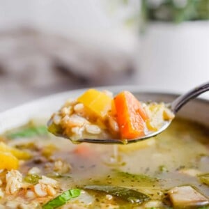 A spoon is lifting the Instant Pot Vegetable Barley Soup out of a bowl.