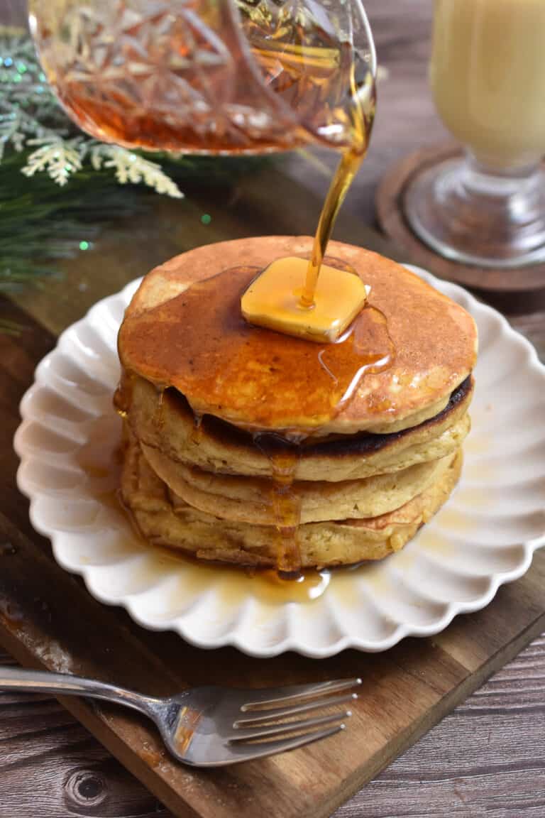 Maple syrup is being poured onto a stack of eggnog pancakes.