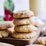 Four cookies are stacked on a cutting board with eggnog in the background.