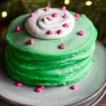 A stack of pancakes has a dollop of whipped cream with heart sprinkles on it.