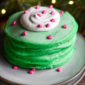 A stack of pancakes has a dollop of whipped cream with heart sprinkles on it.