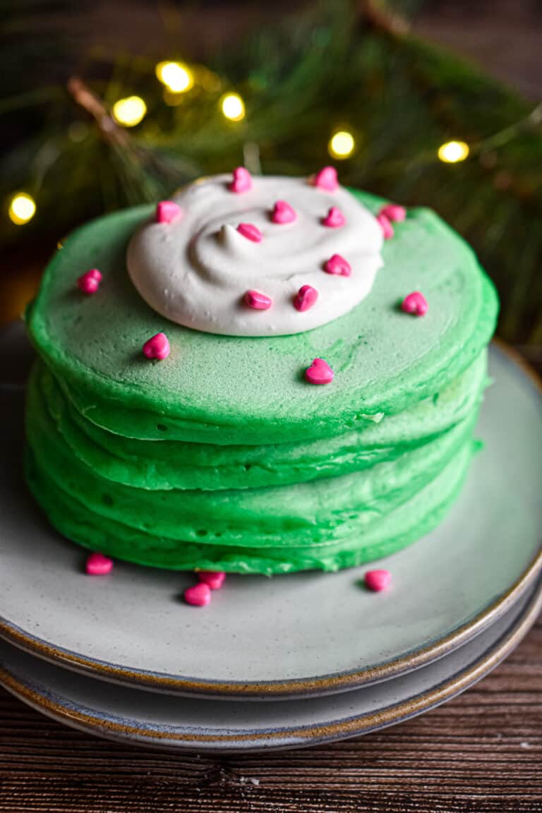 A stack of pancakes has a dollop of whipped cream with heart sprinkles on it.